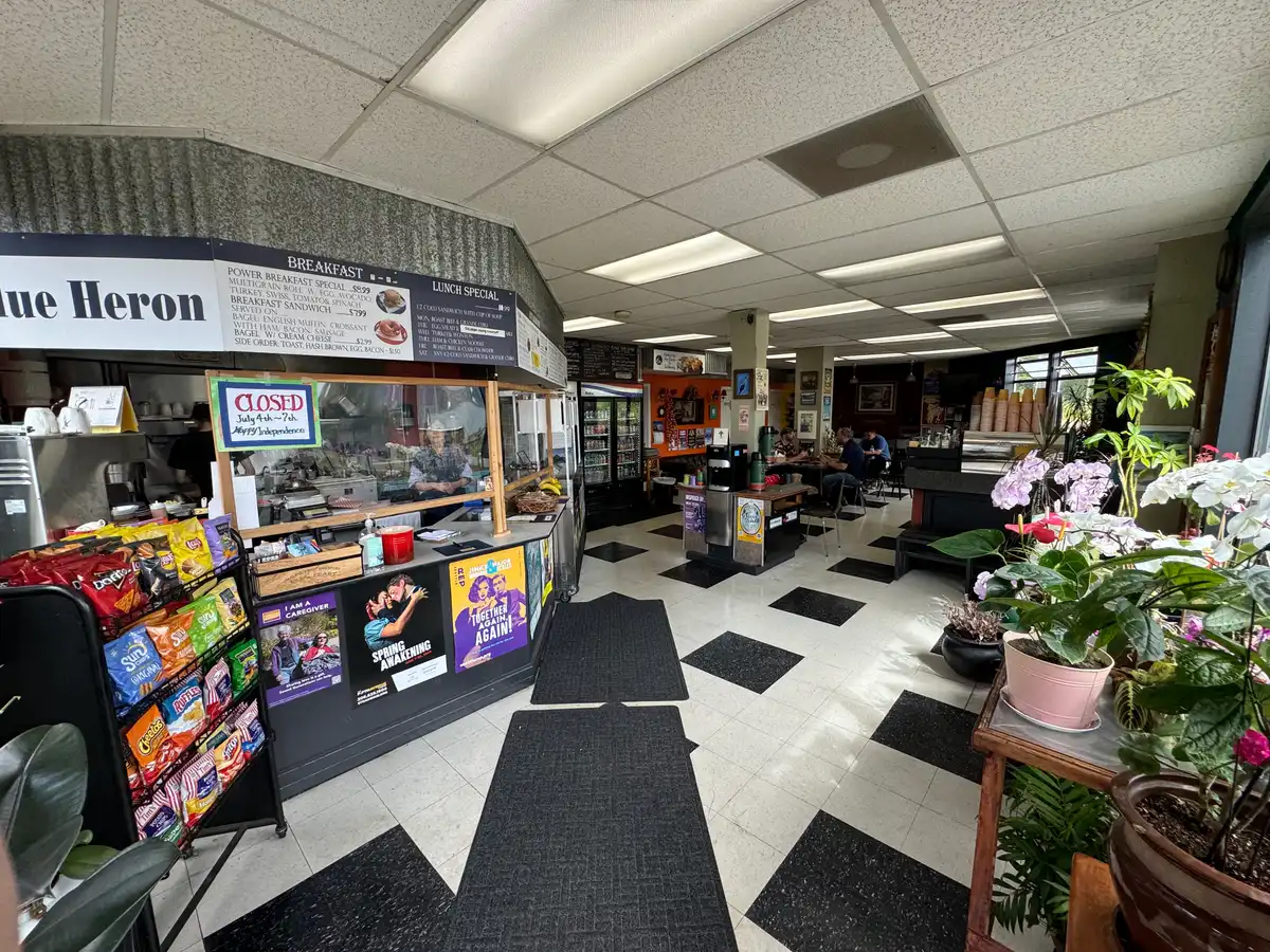 Inside Blue Heron: a black and white checkerboard floor, hand-lettered menu boards above the deli counter, and orchids along the window