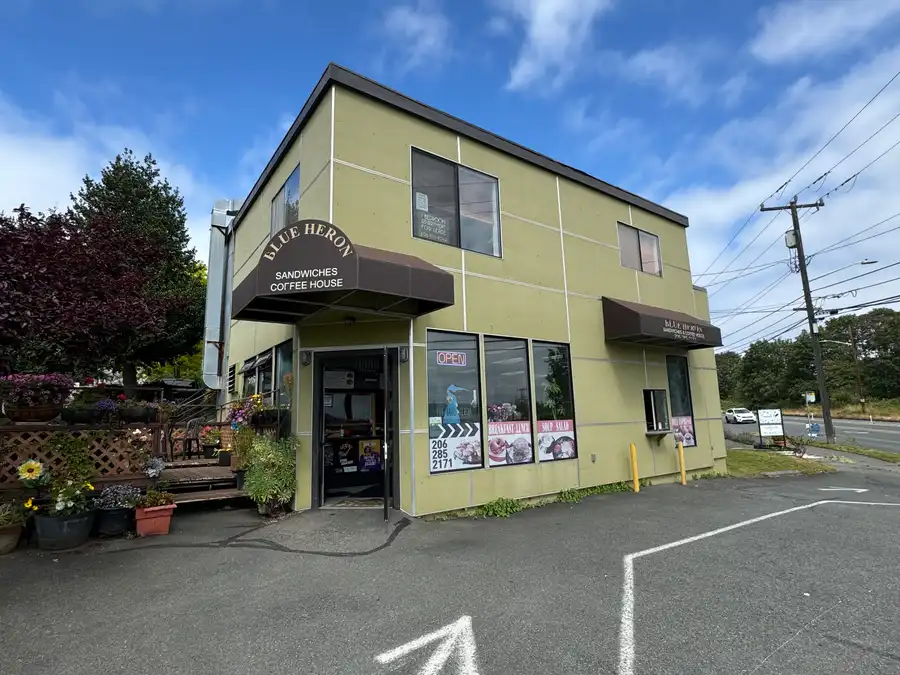 The Blue Heron corner building on Gilman Ave W, with its brown awning and flower pots by the front steps
